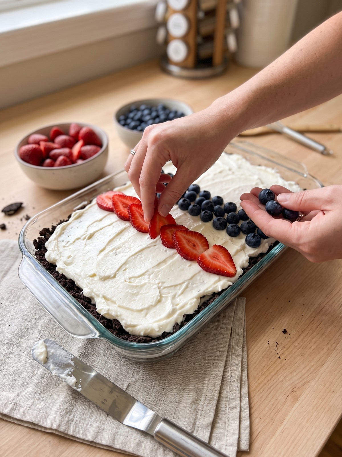 Step-by-step collage showing the chocolate crust being pressed into a dish, the cream cheese mixture being spread, and the strawberry and blueberry sauces being layered.